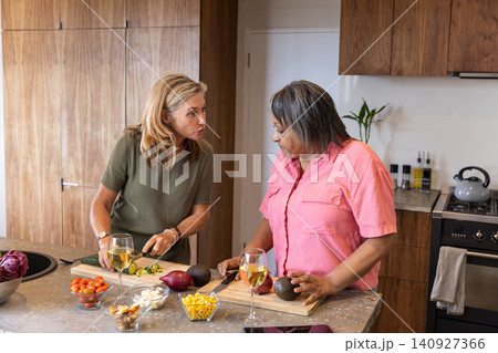 Diverse female friends chopping zucchini and avocado on granite kitchen island in kitchen Diverse female friends chopping zucchini and avocado on granite kitchen island in kitchen 140927366