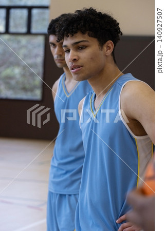 Diverse male teammates in blue jerseys standing with basketball near padded wall in gym court Diverse male teammates in blue jerseys standing with basketball near padded wall in gym court 140927507