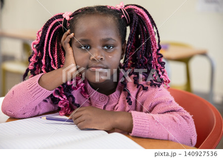 African american child in pink sweater sitting at desk in classroom with notebook and pencil African american child in pink sweater sitting at desk in classroom with notebook and pencil 140927536