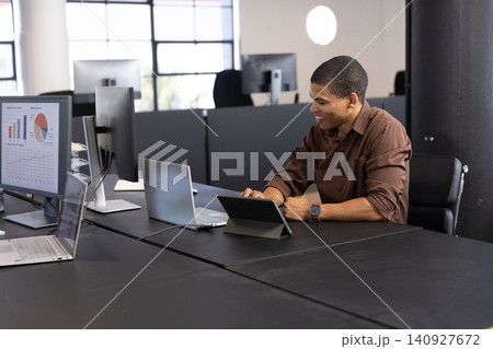 African american man typing on tablet as monitor displaying charts at office, copy space 140927672