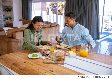 Diverse couple eating breakfast at home dining table with scrambled eggs, orange juice 140927721