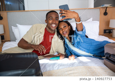 African American couple lying on hotel bed raising smartphone smiling with passports and suitcase African American couple lying on hotel bed raising smartphone smiling with passports and suitcase 140927753