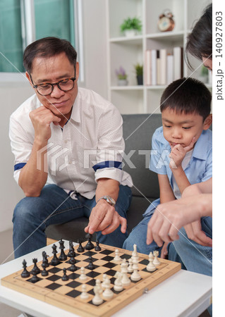 Asian grandfather teaching grandson how to play chess at home for cognitive development 140927803