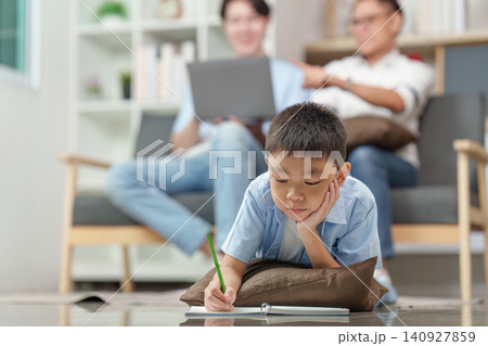 Asian boy doing homework on floor with father and grandfather in background 140927859