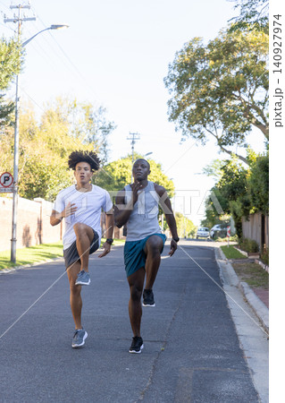 Diverse male friends running high-knee drills wearing fitness watches on street 140927974