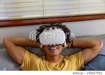 African american man reclining on light grey couch at home using vr headset 140927991