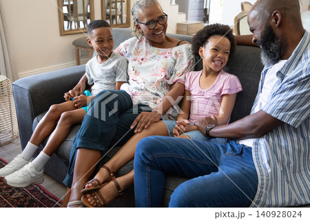 African American family sharing turquoise toy while sitting together on grey sofa in living room African American family sharing turquoise toy while sitting together on grey sofa in living room 140928024