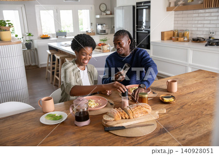 African american couple seasoning scrambled eggs with pepper and salt grinders at table in kitchen African american couple seasoning scrambled eggs with pepper and salt grinders at table in kitchen 140928051