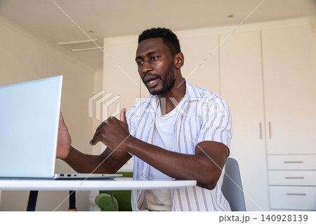 African american man at round table in apartment gesturing in online meeting with laptop African american man at round table in apartment gesturing in online meeting with laptop 140928139