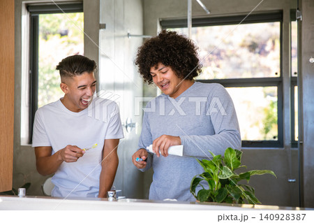 Diverse male friends brushing teeth with toothbrushes and toothpaste tube by bathroom sink 140928387