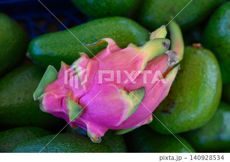 Vibrant dragon fruit contrasts with a mound of ripe avocados in a bustling market during a sunny afternoon 140928534