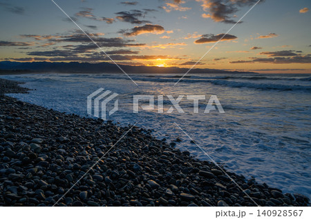 Sunset casts golden hues over rocky shoreline with gentle waves lapping at dusk Sunset casts golden hues over rocky shoreline with gentle waves lapping at dusk 140928567