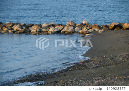 Coastal tranquility unfolds with gentle waves lapping against rocky shoreline at sunset 140928575