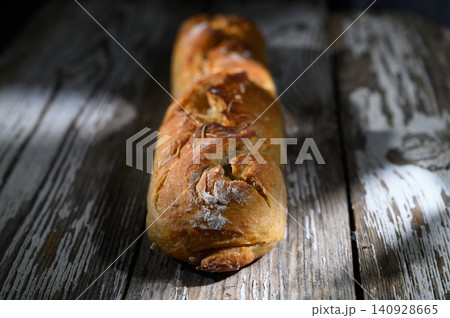 Rustic loaf of bread resting on weathered wooden table under soft light Rustic loaf of bread resting on weathered wooden table under soft light 140928665