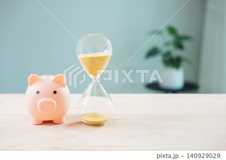 Save money in piggy bank, invest dividend income for interest fund pig, hourglass sand signifies time management for financial growth on wooden table with blurred plant background Save money in piggy bank, invest dividend income for interest fund pig, hourglass sand signifies time management for financial growth on wooden table with blurred plant background 140929029