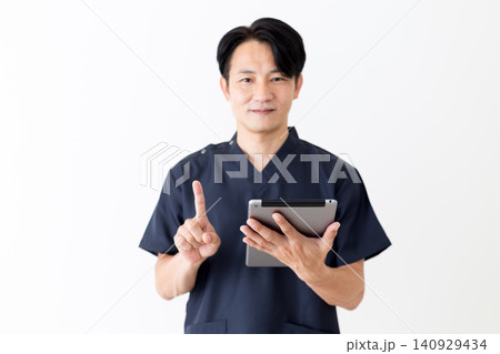 タブレットを持って人差し指を立てる紺色のスクラブを着たミドル男性医師 タブレットを持って人差し指を立てる紺色のスクラブを着たミドル男性医師 140929434