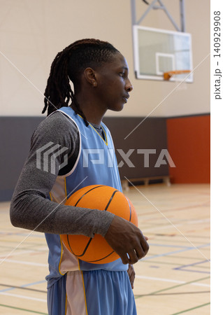 African American male holding basketball and facing right on gym hardwood court with hoop visible African American male holding basketball and facing right on gym hardwood court with hoop visible 140929908