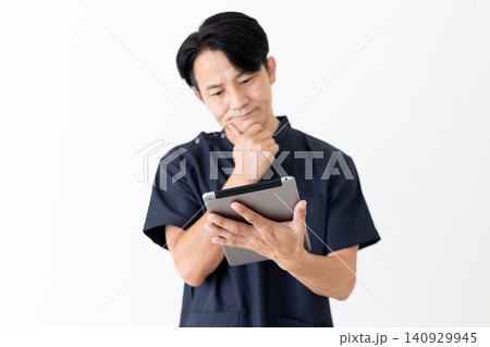 タブレットを見て悩む紺色のスクラブを着たミドル男性医師 タブレットを見て悩む紺色のスクラブを着たミドル男性医師 140929945