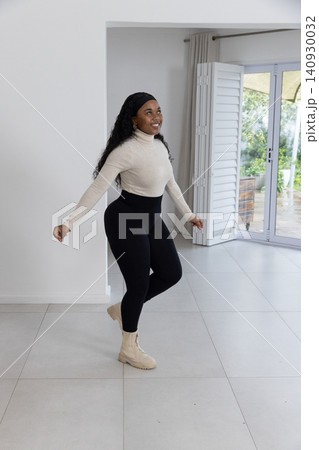 African American woman smiling, balancing foot in home wearing beige boots near sliding doors 140930032