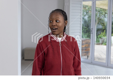 Adult African American woman standing at home by sliding glass doors, wearing red jacket, nose stud 140930034