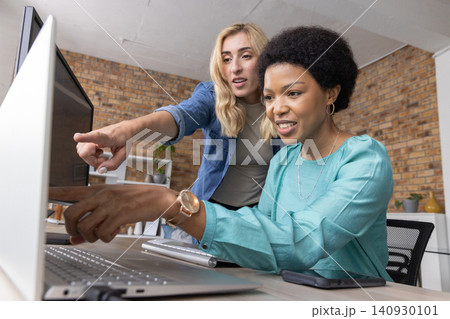 Diverse female coworkers collaborating at office African American seated in teal top using monitor 140930101