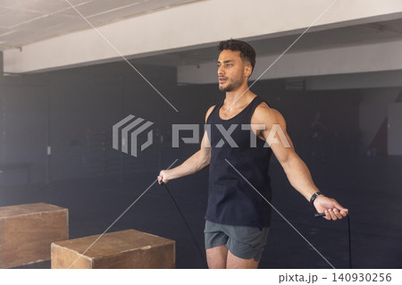 Man skipping rope beside two wooden plyometric boxes in gym wearing fitness watch, copy space 140930256