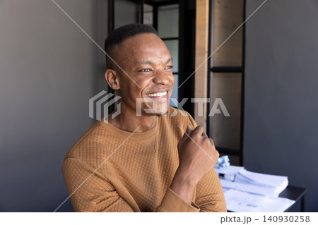 African american man wearing sweatshirt at desk smiling, looking sideways in office with papers 140930258