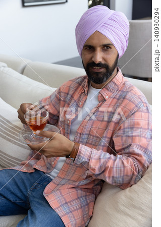 Indian man holding glass teacup sitting on sofa in living room, copy space 140930294