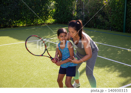 Asian mother and daughter wearing sportswear on private court and guiding grip on racket 140930315