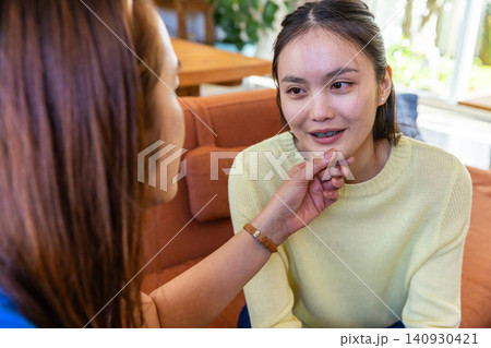 Asian mother comforting teenage daughter on couch by window with houseplant 140930421