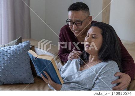 Diverse couple sitting on tan leather sofa in living room reading hardcover book with eyeglasses Diverse couple sitting on tan leather sofa in living room reading hardcover book with eyeglasses 140930574