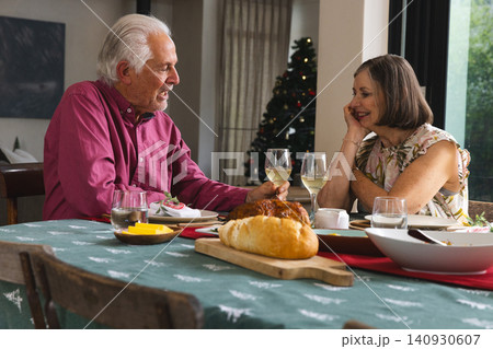 Senior couple toasting Christmas meal with wine glasses at home dining table with Christmas tree 140930607