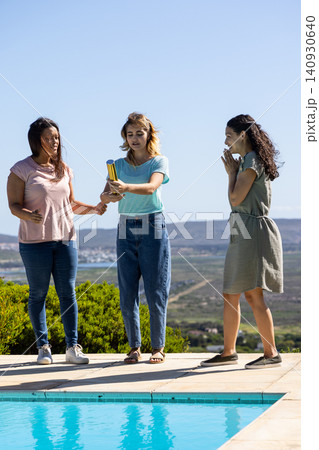 Diverse female friends passing metallic baton on tiled pool deck overlooking valley with pool Diverse female friends passing metallic baton on tiled pool deck overlooking valley with pool 140930640