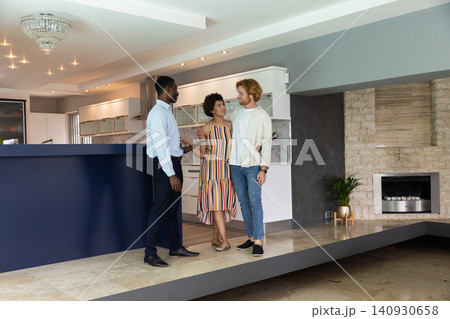 Diverse real estate agent and clients touring open-concept kitchen with island 140930658