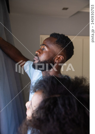 African american couple standing by window pulling back curtains at home, ceiling vent African american couple standing by window pulling back curtains at home, ceiling vent 140930703