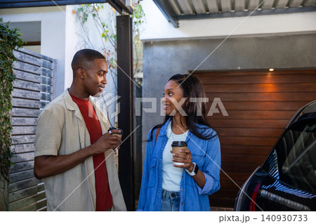 African American couple chatting beside parked car under metal carport holding takeaway coffee cups 140930733
