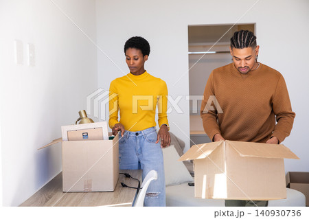 African American couple unpacking cardboard boxes at wooden desk in apartment room with brass lamp African American couple unpacking cardboard boxes at wooden desk in apartment room with brass lamp 140930736
