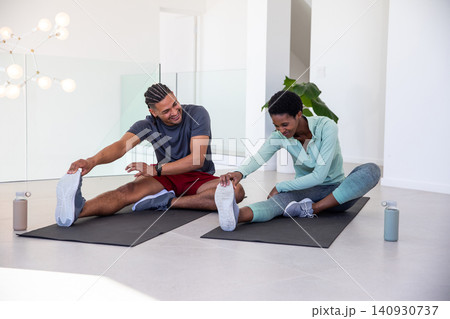 Diverse workout partners reaching forward grasping toes on yoga mats in studio with water bottles Diverse workout partners reaching forward grasping toes on yoga mats in studio with water bottles 140930737