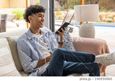Man speaking into smartphone while sitting on sofa near lamp in living room Man speaking into smartphone while sitting on sofa near lamp in living room 140930860