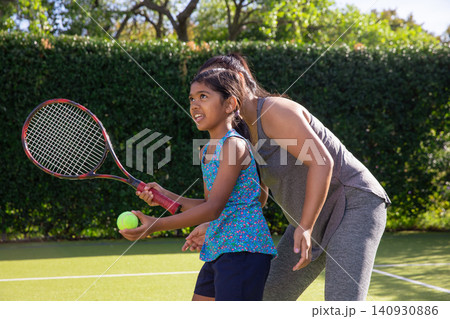 Asian instructor and child practicing on tennis court in sportswear holding racket, tennis ball Asian instructor and child practicing on tennis court in sportswear holding racket, tennis ball 140930886