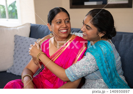 Indian mother and daughter hugging while smiling on dark blue upholstered sofa in living room Indian mother and daughter hugging while smiling on dark blue upholstered sofa in living room 140930897