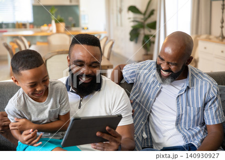African American family sharing digital tablet and laughing on gray sofa in open-plan living area 140930927