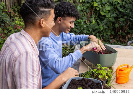 Two male friends filling planter with soil, planting seedlings at backyard table Two male friends filling planter with soil, planting seedlings at backyard table 140930932
