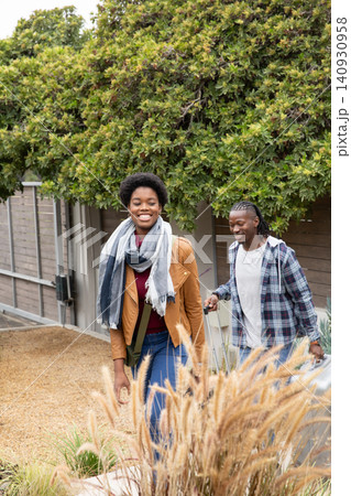 African american couple walking along front yard pulling silver suitcase carrying crossbody bag 140930958