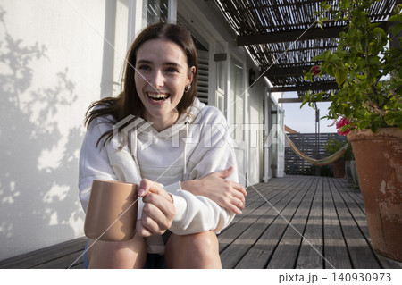 Woman holding large ceramic mug and smiling on wooden veranda under slatted pergola, copy space Woman holding large ceramic mug and smiling on wooden veranda under slatted pergola, copy space 140930973