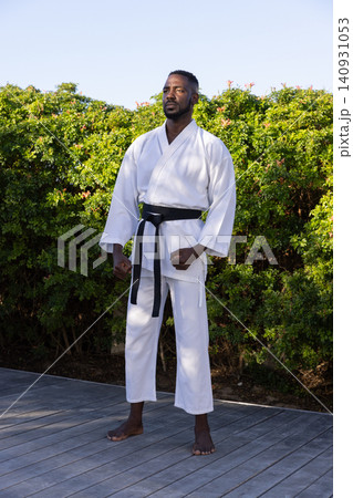 African american man practicing martial arts stance wearing white gi and black belt on deck 140931053