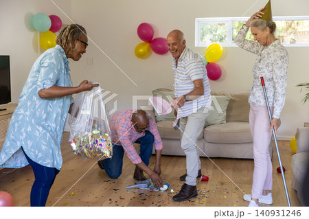 Diverse senior friends tidying living room after party, collecting confetti with dustpan Diverse senior friends tidying living room after party, collecting confetti with dustpan 140931246