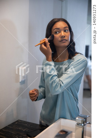 African american woman applying blush with brush at bathroom sink with open palette African american woman applying blush with brush at bathroom sink with open palette 140931273