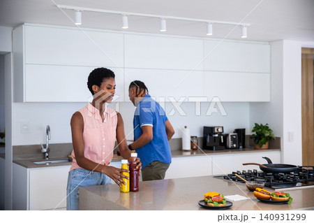 Diverse couple holding mustard and ketchup bottles while preparing sandwich buns on kitchen island Diverse couple holding mustard and ketchup bottles while preparing sandwich buns on kitchen island 140931299