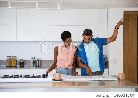 African American couple reviewing large architectural blueprints on kitchen island with coffee mugs African American couple reviewing large architectural blueprints on kitchen island with coffee mugs 140931304